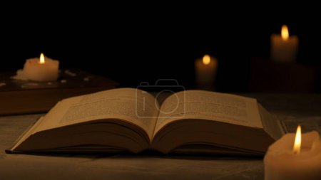 Photo for Historical and vintage objects creative advertisement concept. Studio shot of old retro hardcover book on dark background in warm light. Old vintage book laying opened with candles around it. - Royalty Free Image