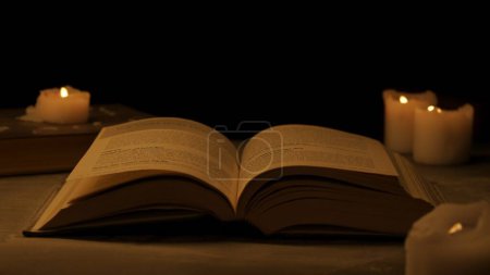 Photo for Historical and vintage objects creative advertisement concept. Studio shot of old retro hardcover book on dark background in warm light. Big old vintage book laying opened on table, candles around it. - Royalty Free Image