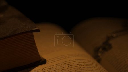Photo for Historical and vintage objects creative advertisement concept. Studio shot of old retro hardcover book on dark background in warm light. Old vintage book in dark light with cross laying opened. - Royalty Free Image