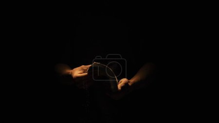 Photo for Historical and vintage objects creative advertisement concept. Studio shot of old retro hardcover book on dark background in warm light. Man holding bending old book in hands. - Royalty Free Image