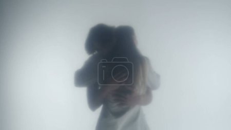 Téléchargez les photos : Silhouette d'un couple embrassant derrière un rideau givré ou un verre fermé. Un homme avec un torse nu et une femme serrant les bras. Une rencontre d'amoureux à travers le temps et l'espace - en image libre de droit