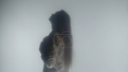 Foto de Vista lateral de silueta de mujer. Una mujer en vapor o niebla detrás de un vidrio esmerilado transparente o una cortina - Imagen libre de derechos