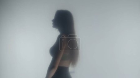 Téléchargez les photos : Vue latérale de la silhouette de la femme en soutien-gorge. Femme dans la vapeur ou le brouillard derrière verre givré transparent ou rideau - en image libre de droit