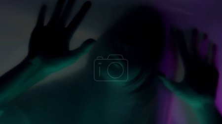 Téléchargez les photos : Silhouette floue d'une femme derrière un rideau mat, en néon rose et vert, gros plan. Une femme se gratte les ongles sur la barrière, essayant de la déchirer. Le concept des fantômes et des esprits - en image libre de droit