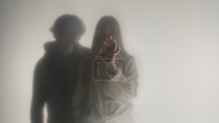 Photo for Silhouette of a man and a woman behind a frosted curtain or glass close up. A man approaches and puts his arm around the shoulders of a pensive and aloof woman drawing patterns on a frosted surface - Royalty Free Image