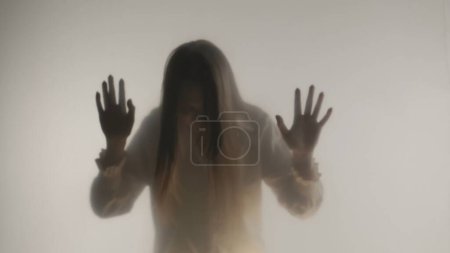Photo for Silhouette of panicked woman in fog behind frosted glass or curtain. The woman bangs her head against a transparent, invisible barrier. Concept of the afterlife and the otherworld, ghosts and spirits - Royalty Free Image