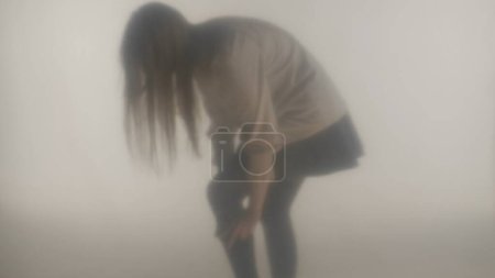 Téléchargez les photos : Silhouette d'une femme dans la vapeur ou le brouillard, derrière un verre dépoli. La femme enlève un bas de sa jambe - en image libre de droit