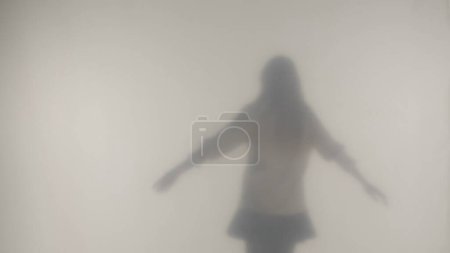Téléchargez les photos : La silhouette d'une femme dansant et tournoyant dans la brume derrière un verre givré ou un rideau. Concept de l'au-delà et de l'au-delà, fantômes et esprits - en image libre de droit