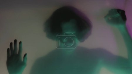 Téléchargez les photos : Une silhouette floue d'un homme avec un torse nu derrière un rideau mat, dans la lumière verte néon fermer. L'homme touche la barrière transparente, essayant de se libérer. Le concept de fantômes et - en image libre de droit