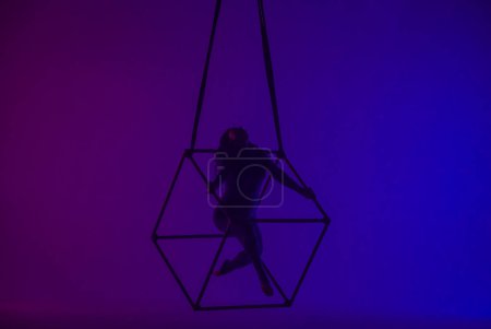 Téléchargez les photos : Silhouette de gymnaste aérienne femelle isolée sur fond néon violet bleu. acrobate féminin performant dans les airs sur un cube, montrant sa flexibilité - en image libre de droit