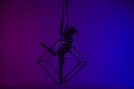 Téléchargez les photos : Silhouette de gymnaste aérienne femelle isolée sur fond néon violet bleu. acrobate féminin performant dans les airs sur un cube, montrant sa flexibilité - en image libre de droit