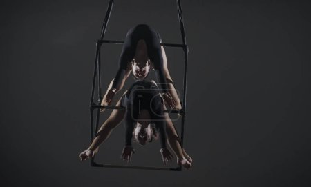 Photo for Trio of young female acrobats posing on a cube suspended at a height. Aerial gymnasts perform in studio against dark background and demonstrate flexibility and stretching. The concept of a circus show - Royalty Free Image