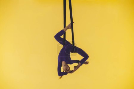 Photo for Modern choreography and acrobatics creative advertisement concept. Female gymnast isolated on yellow studio background. Girl aerial dancer spinning on gymnastic straps, showing acrobatic elements. - Royalty Free Image