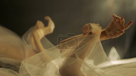 Photo for Hands of a woman with white tulle on a black background close up. A mirror reflects the blurred silhouette of a woman covered with netted fabric, illuminated by warm rays of light - Royalty Free Image