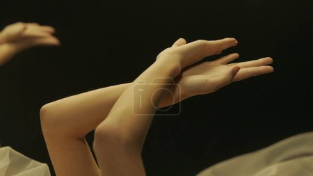 Téléchargez les photos : Les femmes mains dans la lumière chaude sur un fond noir réfléchi dans un miroir, fermer. Concept de soins de la peau - en image libre de droit