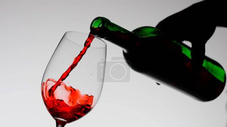 Photo for Food and drink advertisement concept. Close up shot of wine glass isolated on white background in studio. Female holding bottle and spilling red wine into a glass creating splashes. - Royalty Free Image
