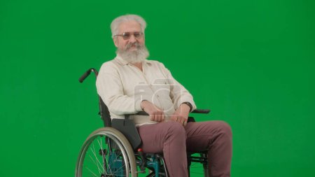 Photo for Pensioner caregiving and everyday life creative advertisement concept. Portrait of aged disabled man on chroma key green screen. Elderly man sits in wheelchair and smiles at the camera. - Royalty Free Image