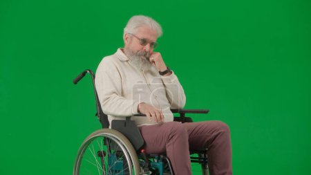 Photo for Pensioner everyday life creative advertisement concept. Portrait of aged man on chroma key green screen background. Elderly man sitting in a wheelchair, thoughtfully propping his head with his hand. - Royalty Free Image