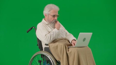 Photo for Pensioner everyday life creative advertisement concept. Portrait of aged man isolated on chroma key green screen background. Senior man in wheelchair covered by plaid watching video on laptop. - Royalty Free Image
