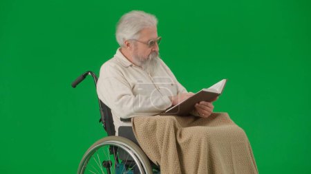 Photo for Pensioner everyday life creative advertisement concept. Portrait of aged man isolated on chroma key green screen background. Senior man in wheelchair covered by plaid reading book. - Royalty Free Image