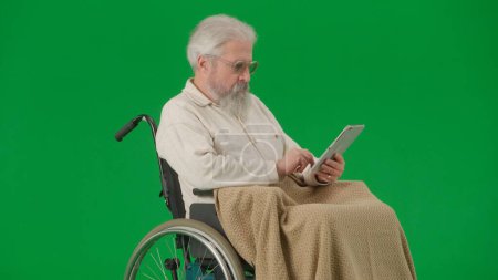 Téléchargez les photos : Pensionné vie quotidienne concept publicitaire créatif. Portrait d'un homme âgé isolé sur fond vert chromatique. Homme âgé en fauteuil roulant couvert par le balayage à carreaux sur tablette. - en image libre de droit