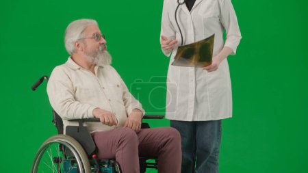 Téléchargez les photos : Pensionné vie quotidienne concept publicitaire créatif. Portrait d'un homme âgé isolé sur fond vert chromatique. Homme âgé en fauteuil roulant parlant avec une femme médecin à la clinique. - en image libre de droit