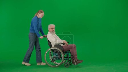 Photo for Pensioner everyday life creative advertisement concept. Portrait of aged man on chroma key green screen background. Young girl walks and carries senior man granddad on a wheelchair. - Royalty Free Image