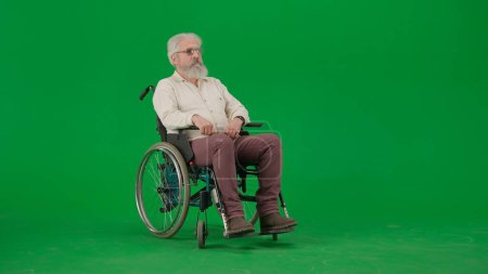 Photo for Pensioner everyday life creative advertisement concept. Portrait of aged man on chroma key green screen background. Senior man sitting in wheelchair looking away from the camera. - Royalty Free Image