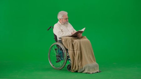 Photo for Pensioner everyday life creative advertisement concept. Portrait of aged man isolated on chroma key green screen background. Senior man in wheelchair covered by plaid reading book. - Royalty Free Image