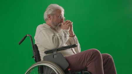 Photo for Pensioner everyday life creative advertisement concept. Portrait of disabled man isolated on chroma key green screen close up. Senior man sitting in wheelchair thinking, holding hands crossed. - Royalty Free Image