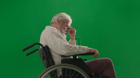 Téléchargez les photos : Pensionné vie quotidienne concept publicitaire créatif. Portrait d'un homme handicapé isolé sur écran vert chromatique de près. Homme âgé assis en fauteuil roulant tenant la main sur le front, pensant. - en image libre de droit