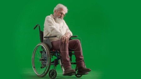 Photo for Pensioner everyday life creative advertisement concept. Portrait of disabled man isolated on chroma key green screen full shot. Senior bearded man in wheelchair touching knee, painful expression. - Royalty Free Image