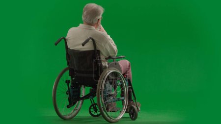 Photo for Pensioner everyday life creative advertisement concept. Portrait of disabled man isolated on chroma key green screen full shot. Senior bearded man sitting in wheelchair with his back at camera. - Royalty Free Image