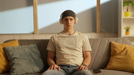 Photo for Music and human emotions creative advertisement concept. Portrait of young person in the room sitting on the couch. Man in headphones listening to music. - Royalty Free Image