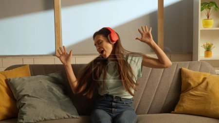 Photo for Music and human emotion creative advertising concept. Woman sitting on a couch listening to music with big red headphones - Royalty Free Image