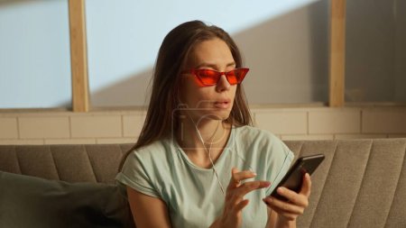 Photo for Music and human emotions creative advertisement concept. Woman in red glasses and earphones on the sofa listening music - Royalty Free Image
