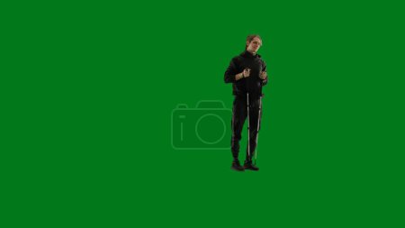 Photo for Half-turned view of a male traveler with trekking poles in his hands. The man is standing full-length and enjoying the view. Hiker in studio on green screen - Royalty Free Image