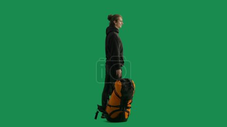 Photo for Side view of a male traveler with a large hiking backpack in his hand. The man is standing full height and enjoying the view. Hiker in studio on green screen - Royalty Free Image