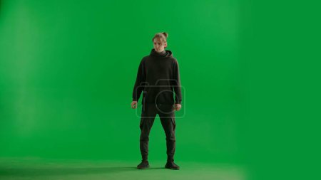 Photo for Male traveler in black tracksuit on green background in studio. The man is standing full height and looking to the side - Royalty Free Image