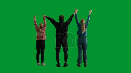 Téléchargez les photos : Vue arrière d'une équipe de trois randonneurs levant les mains en l'air, faisant un geste de victoire. Un groupe de personnes se réjouissant et acclamant dans un studio sur un écran vert. Concept de voyage - en image libre de droit