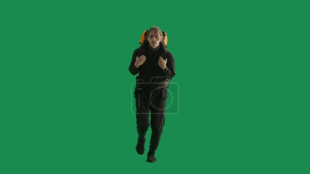 Photo for A male tourist with a backpack on his back walks in the studio on a green screen. Hiking trek rest travel trip concept - Royalty Free Image