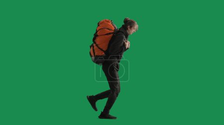 Téléchargez les photos : Vue latérale d'un randonneur masculin en pleine longueur, courant avec un grand sac à dos lourd sur le dos. Voyageur pressé en studio sur écran vert. Dernier moment pour la randonnée et les vacances précipitées - en image libre de droit