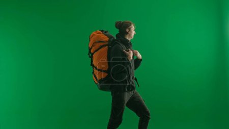 Photo for Half-turned view of a male traveler with a large hiking backpack on his back. The man is standing full-length and enjoying the view. Hiker in studio on green screen - Royalty Free Image