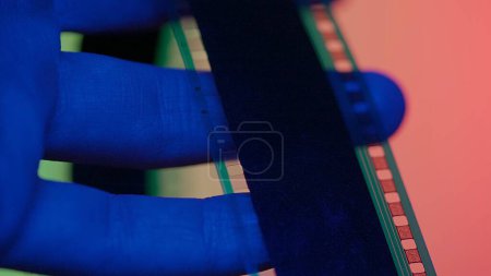 Foto de Revisando una tira de película fotográfica negativa. Película fotográfica en manos de hombre en luz de neón roja, azul y verde de cerca - Imagen libre de derechos