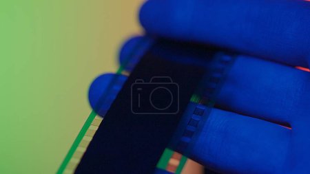 Photo for Reviewing a negative photo film strip. Photographic film in mens hands in red, blue and green neon light close up - Royalty Free Image