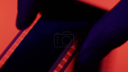 Foto de Silueta de película en mano de hombre sobre fondo rojo de cerca. Textura de película vieja, fácil de usar en composición - Imagen libre de derechos