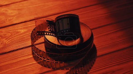 Téléchargez les photos : Torsadé en rouleaux de vieux négatifs de film 35mm sur une table en bois dans le noir gros plan. Les rouleaux de film sont éclairés par une lumière rouge néon - en image libre de droit