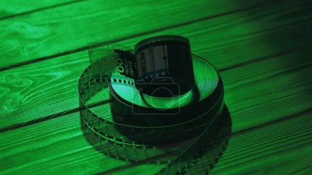 Téléchargez les photos : Torsadé en rouleaux de vieux négatifs de film 35mm sur une table en bois dans le noir gros plan. Les rouleaux de film sont éclairés par une lumière verte au néon - en image libre de droit