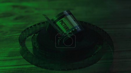 Photo for Twisted into rolls of old 35mm film negatives on a wooden table in the dark close up. The rolls of film are illuminated by a green neon light - Royalty Free Image