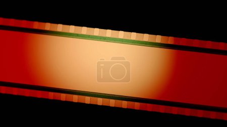 Foto de Tiras de película roja con luz circular naranja sobre fondo negro de cerca. Cinema filmstrip sobre fondo negro. Marco de diapositiva de película de 35 mm. Cinema o marcos de fotos. Marco de tira de película largo y retro. Copiar espacio - Imagen libre de derechos